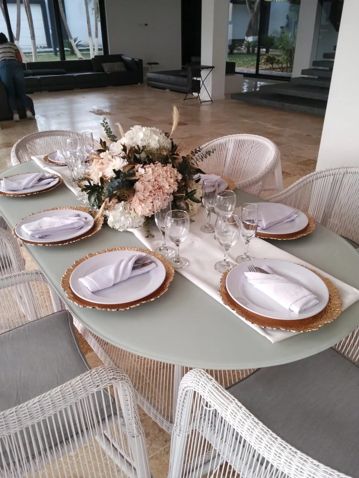 Table dressée en extérieur, chemin de table blanc, sous-assiettes dorées et centre floral