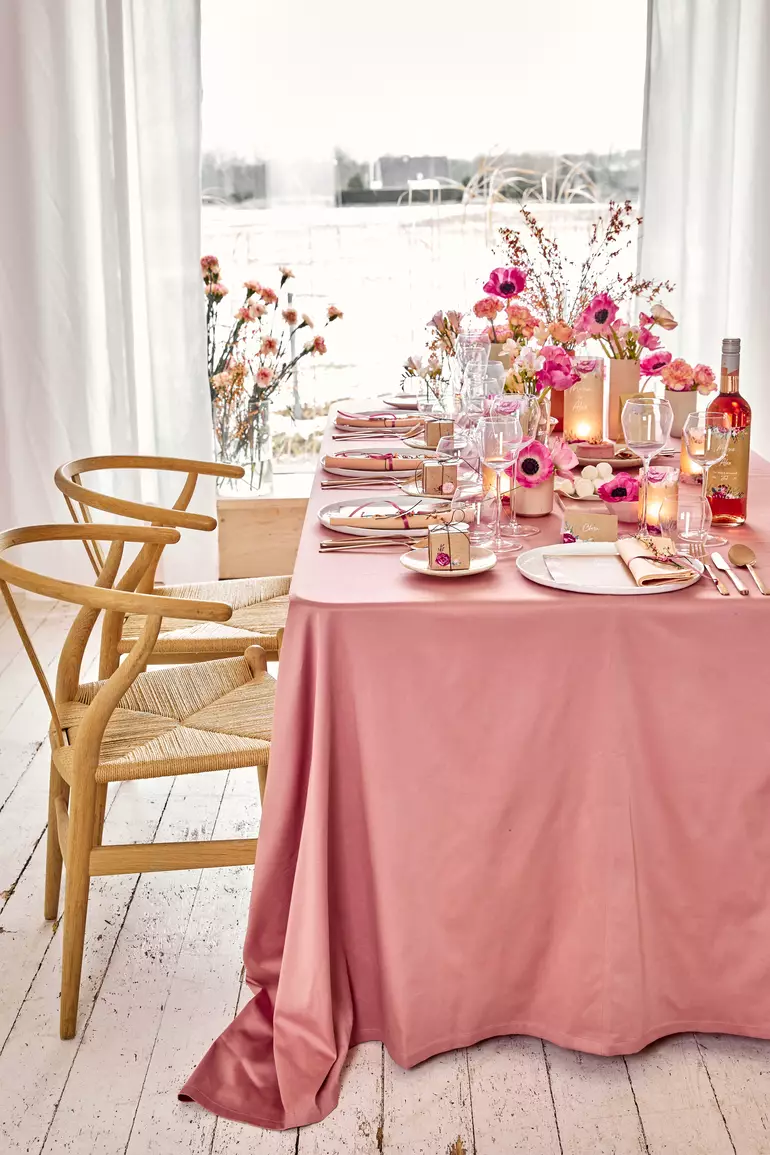 Table dressée élégante avec nappe rose vieilli et compositions de fleurs roses