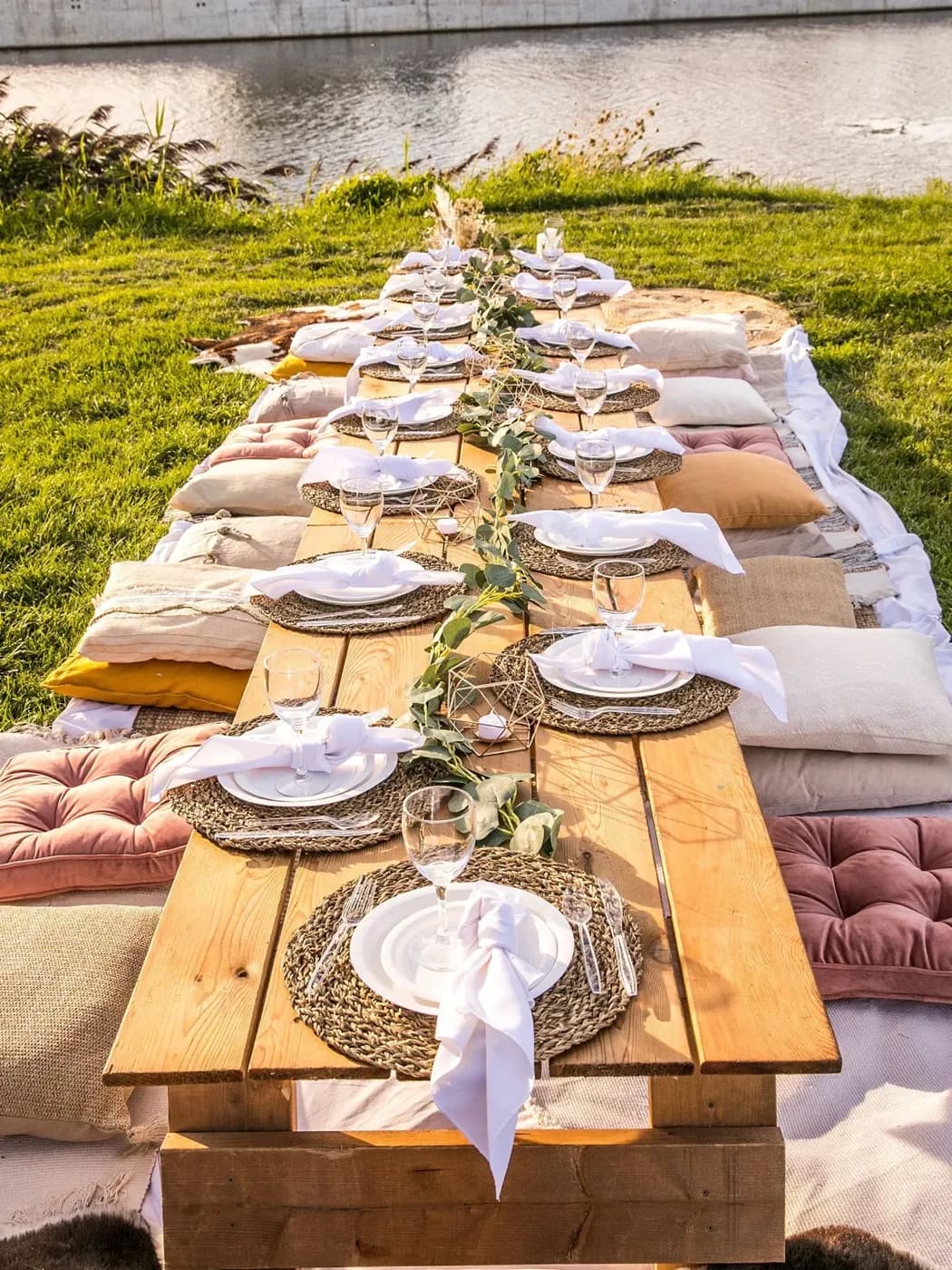 Pique-nique au bord de l'eau, table basse en bois, coussins de sol et chemin de table d'eucalyptus