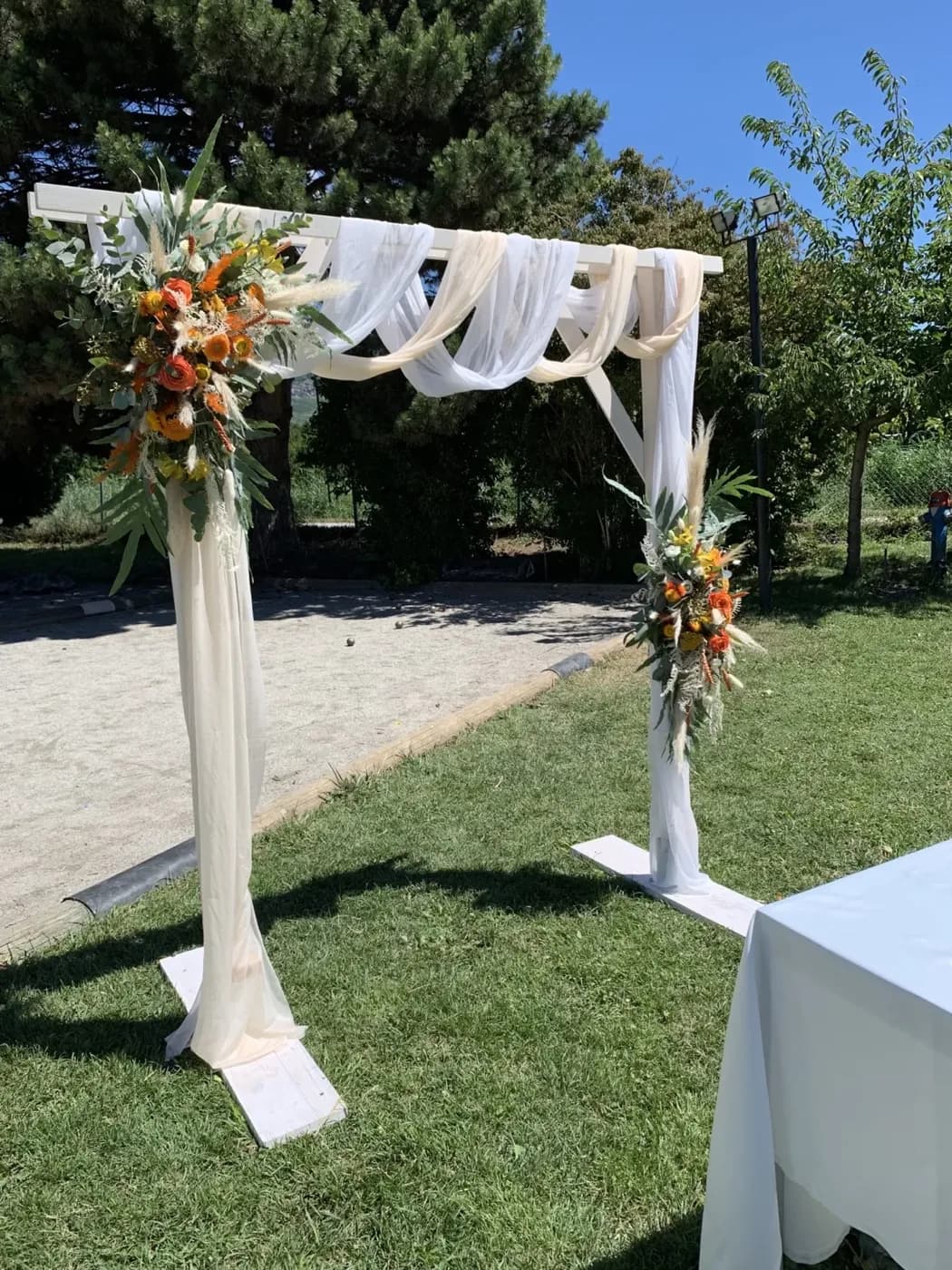 Arche de cérémonie en bois avec voile ivoire drapé et compositions de fleurs séchées orangées